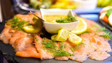 A platter of smoked salmon garnished with dill and lemon slices, accompanied by a small bowl of sauce.