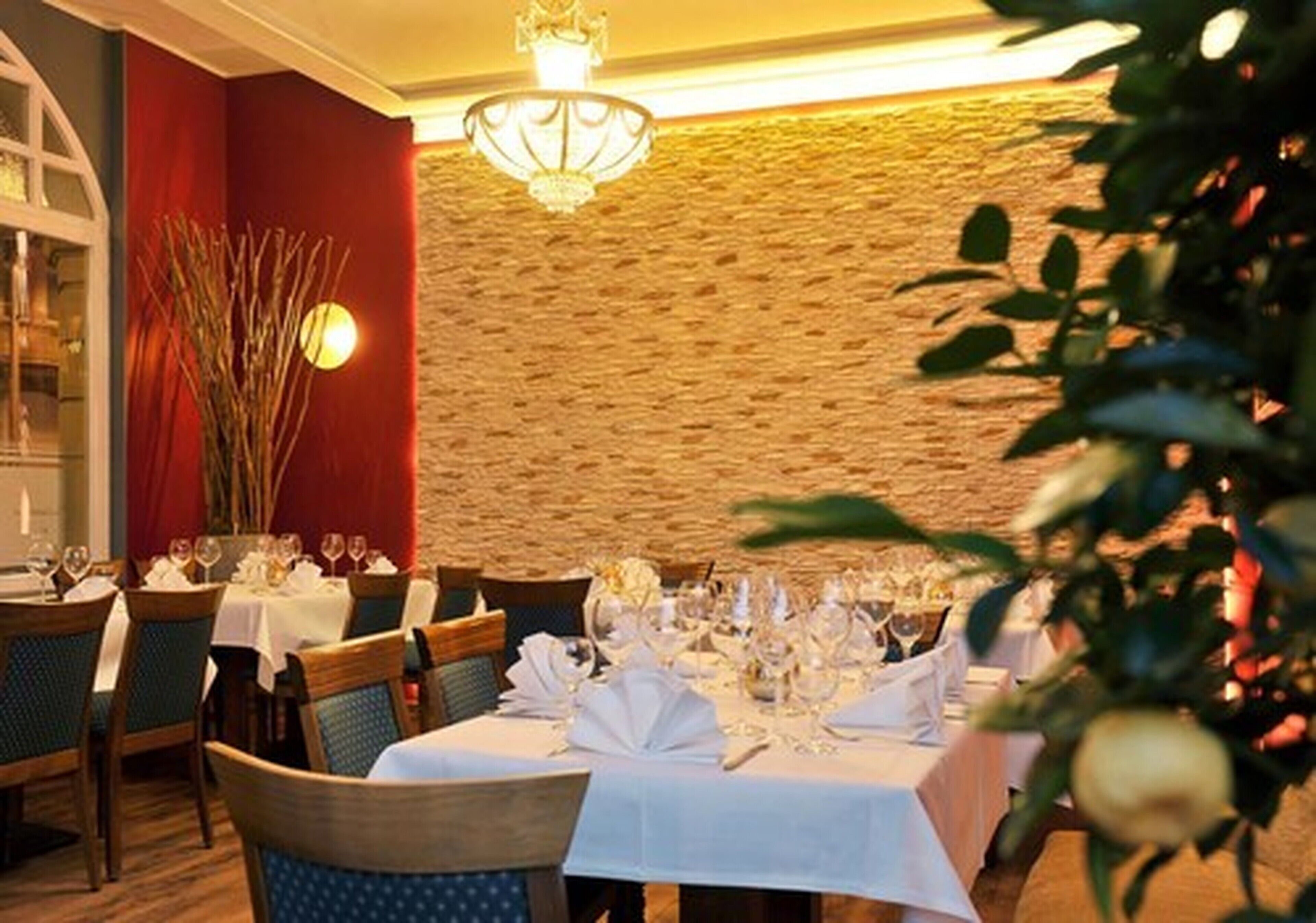 A restaurant with tables set for dining, a chandelier, and a stone wall.