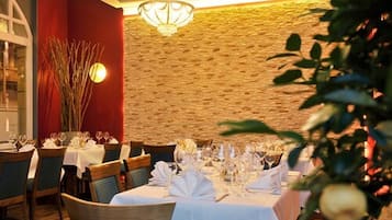A restaurant with tables set for dining, a chandelier, and a stone wall.