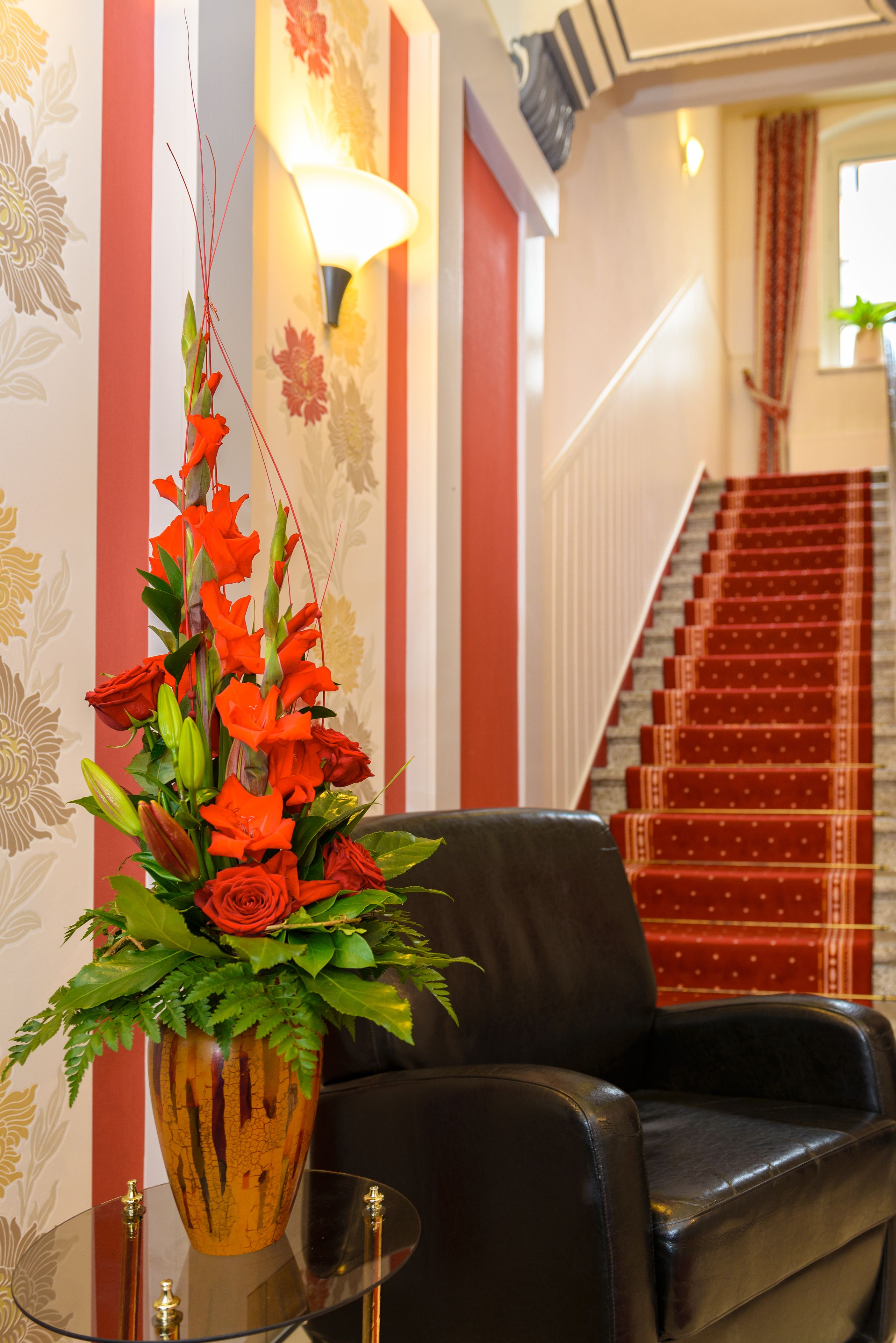 Un vestíbulo de hotel con una pared a rayas rojas y blancas, una escalera con alfombra roja y un sillón de cuero negro.