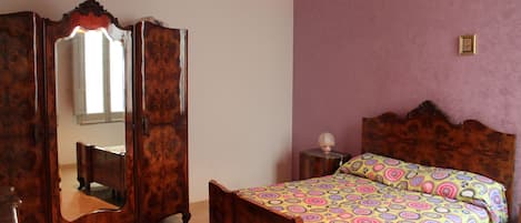 Une chambre avec un lit en bois, un miroir, une lampe suspendue rouge et un mur violet.