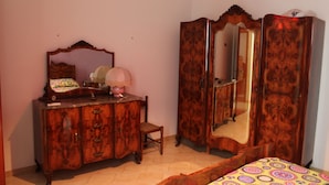 Una camera da letto con un comò in legno, una sedia, un letto con copriletto decorato e un armadietto specchiato.