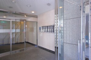 A modern elevator area with glass doors, a control panel, and a tiled wall.