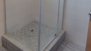 A glass-enclosed shower with a tiled floor and a small window.