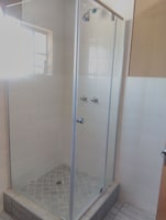 Ducha con mampara de vidrio, suelo de baldosas y una ventana pequeña.