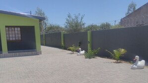 A paved outdoor area with a green building, a high wall with barbed wire, and two swan statues.
