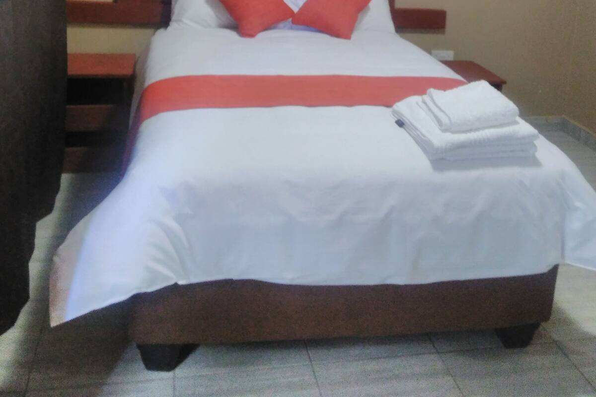 A neatly made bed with a white bedspread, two red pillows, and a red bed runner.