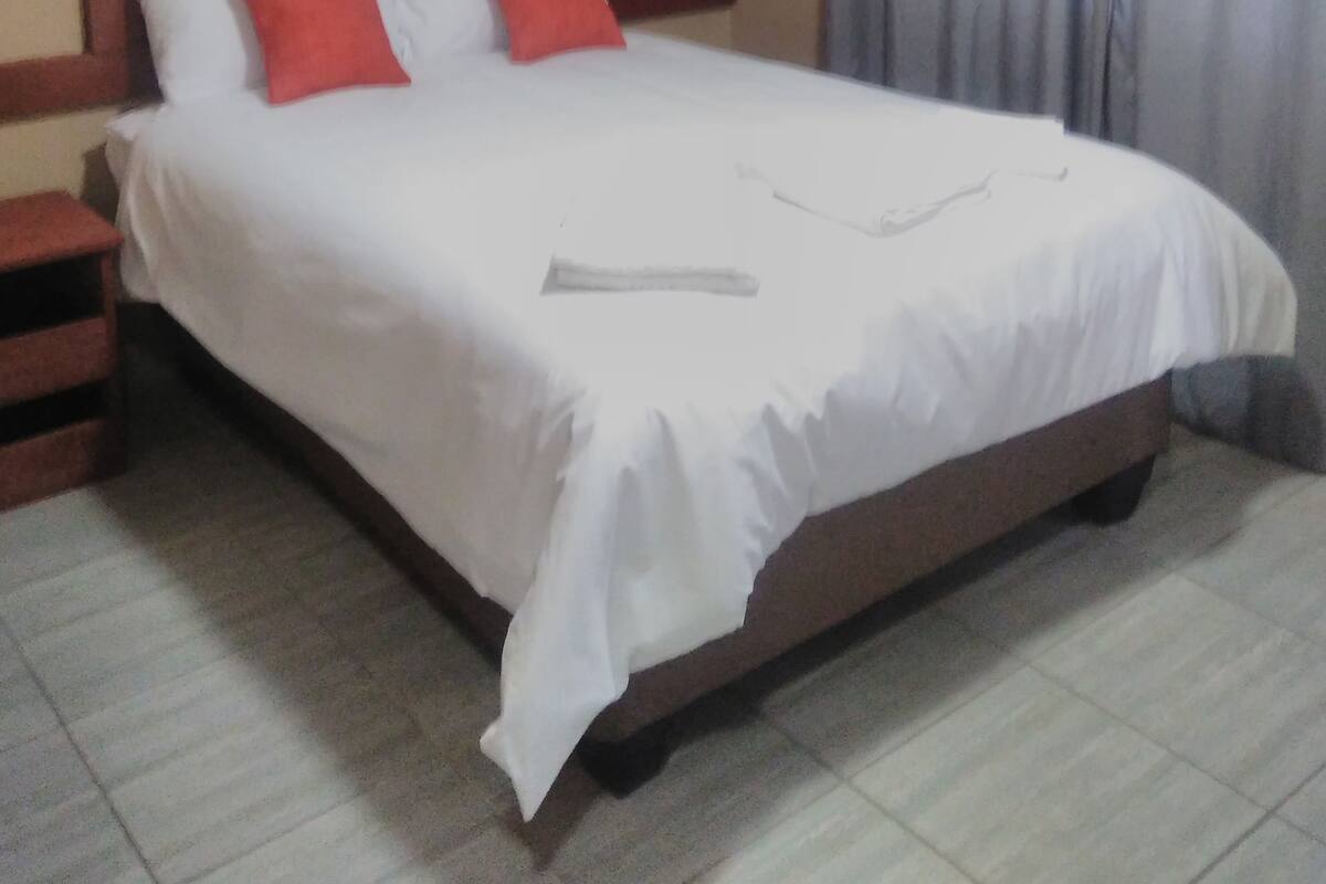 A standard hotel room with a single bed, a nightstand, and a window with curtains.