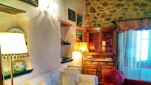 A cozy room with a white sofa, a red armchair, a wooden cabinet with glassware, and a stone wall. - Villa Via Savoia (Leros)