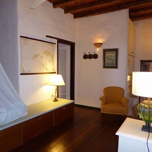 A room with a wooden floor, a bed with a white canopy, a desk with a lamp, a chair, and a wall-mounted globe.