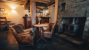A cozy room with leather armchairs, a round table, a bar area, and a stone fireplace. - The Three Shires Inn (Ambleside)