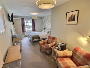 A hotel room with a bed, a desk, a chair, a sofa, a small table with a lamp, and a picture on the wall.