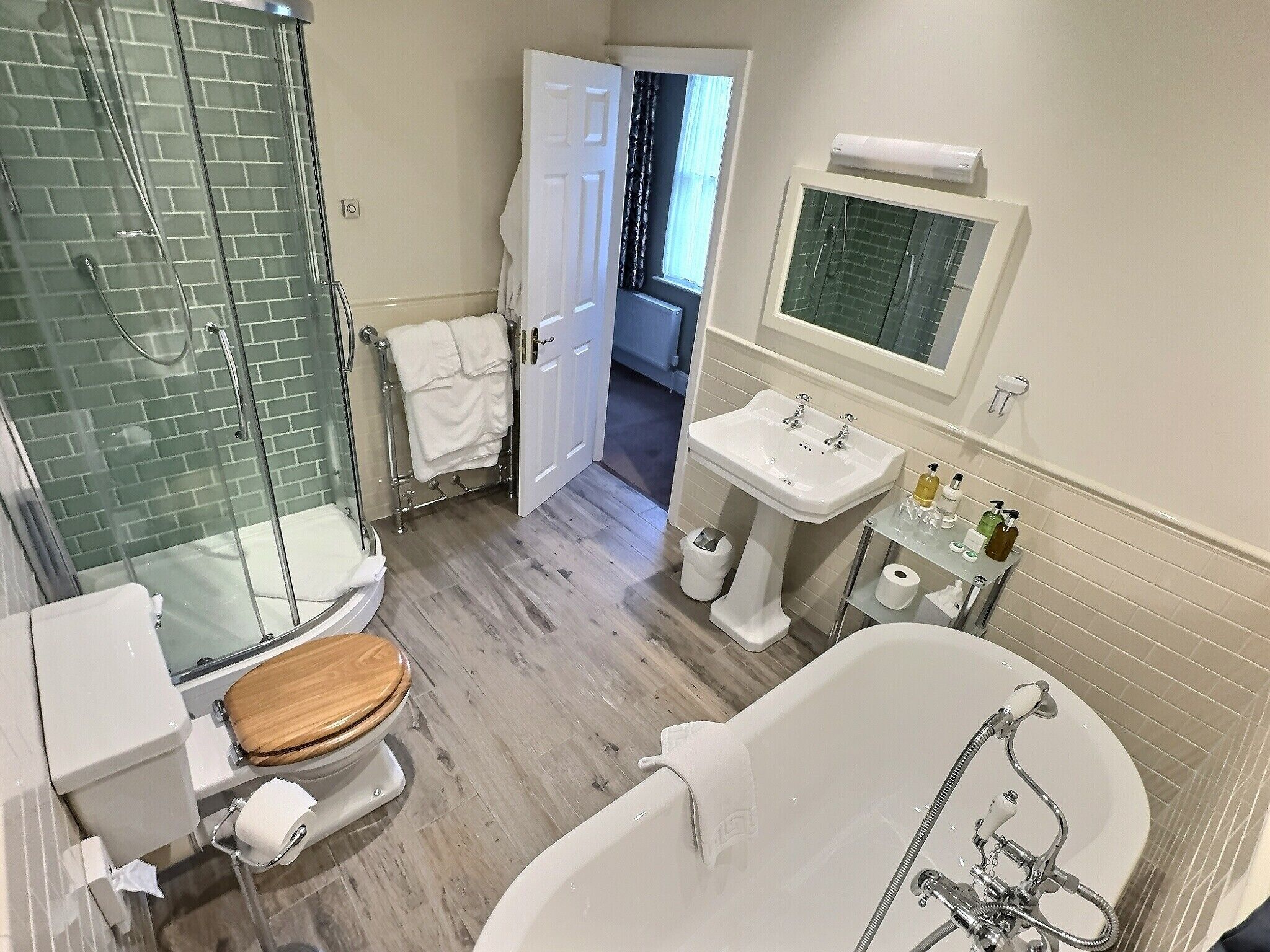 Un baño con cabina de ducha de vidrio, inodoro con asiento de madera, bañera, lavabo y espejo.