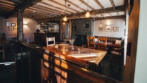 A rustic interior with exposed wooden beams, a long wooden table, and a bar area. - The Three Shires Inn (Ambleside)
