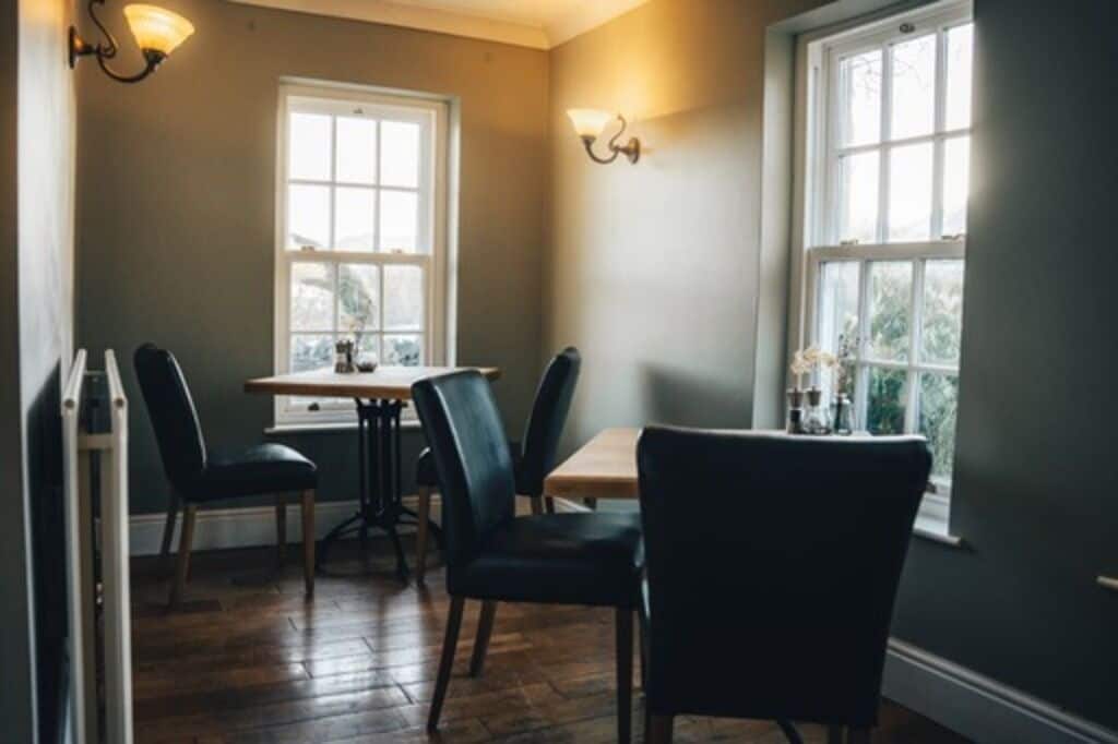 A dining area with a table and chairs, two windows, and wall-mounted light fixtures.
