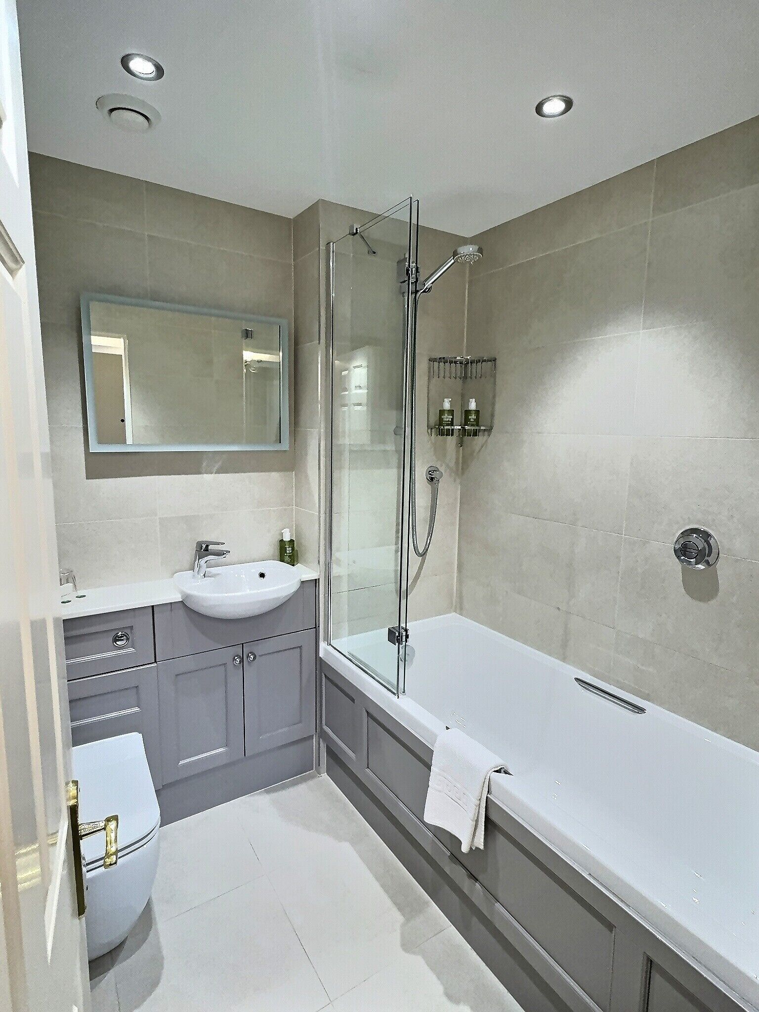 Un baño moderno con ducha de vidrio, una bañera blanca y un tocador con lavamanos y espejo.
