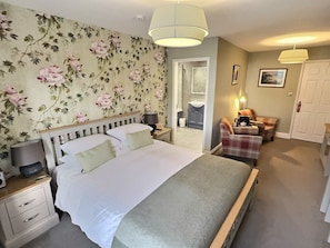 A bedroom with a large bed, a nightstand, a chair, and a bedside table.