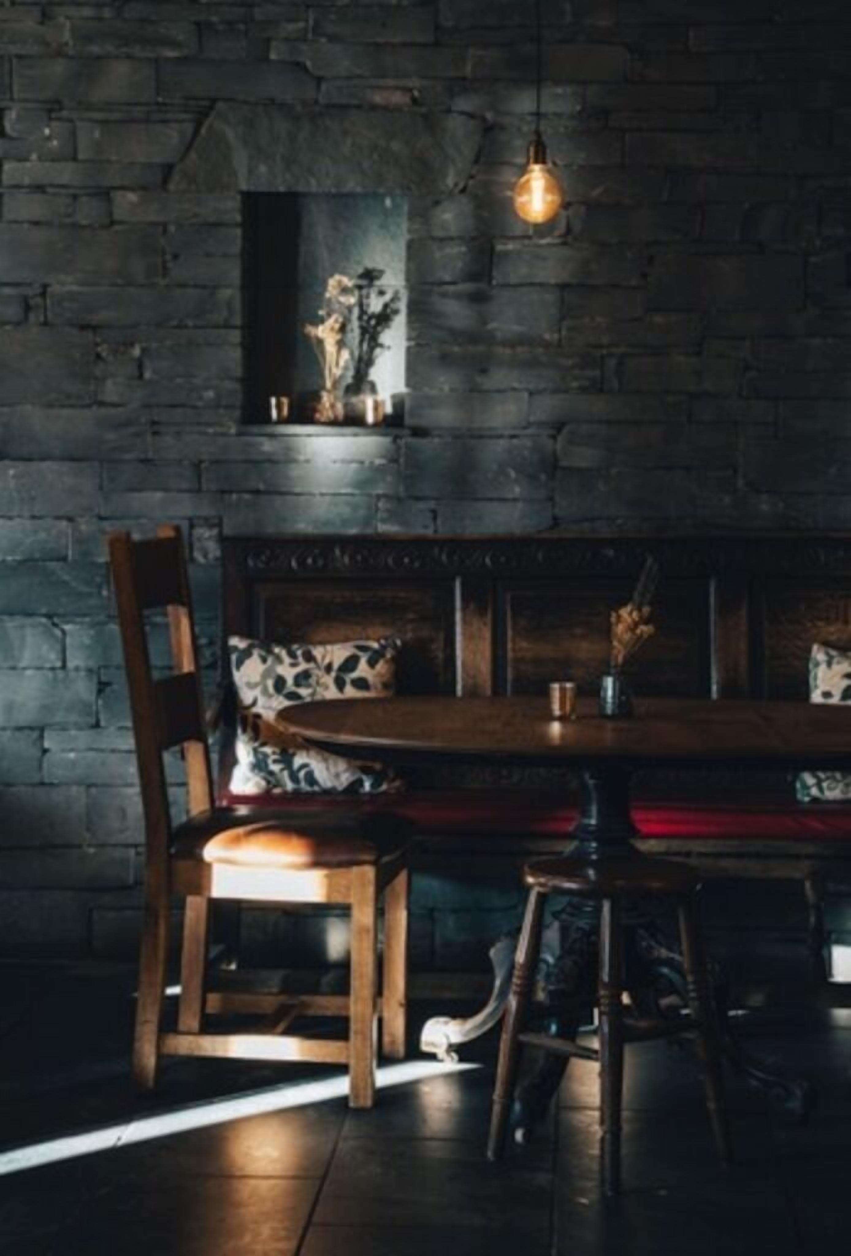 A dimly lit room with a brick wall, a wooden table, and a single hanging light bulb.