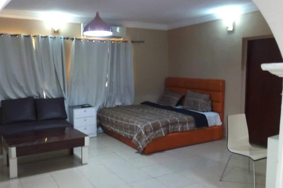 A bedroom with a bed, a bedside table, a chair, and curtains.