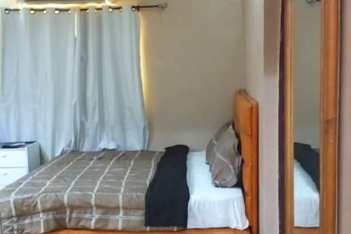 A single bed with a wooden headboard, a bedside table, and a large mirror.