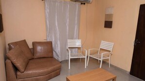 Una habitación pequeña y amoblada con un sofá marrón, dos sillas blancas y una mesa de madera.