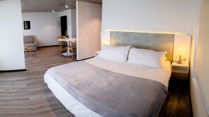 A modern hotel room with a large bed, bedside tables with lamps, a small table with chairs, and a view of the adjacent living area. - hUB Antofagasta (Antofagasta)