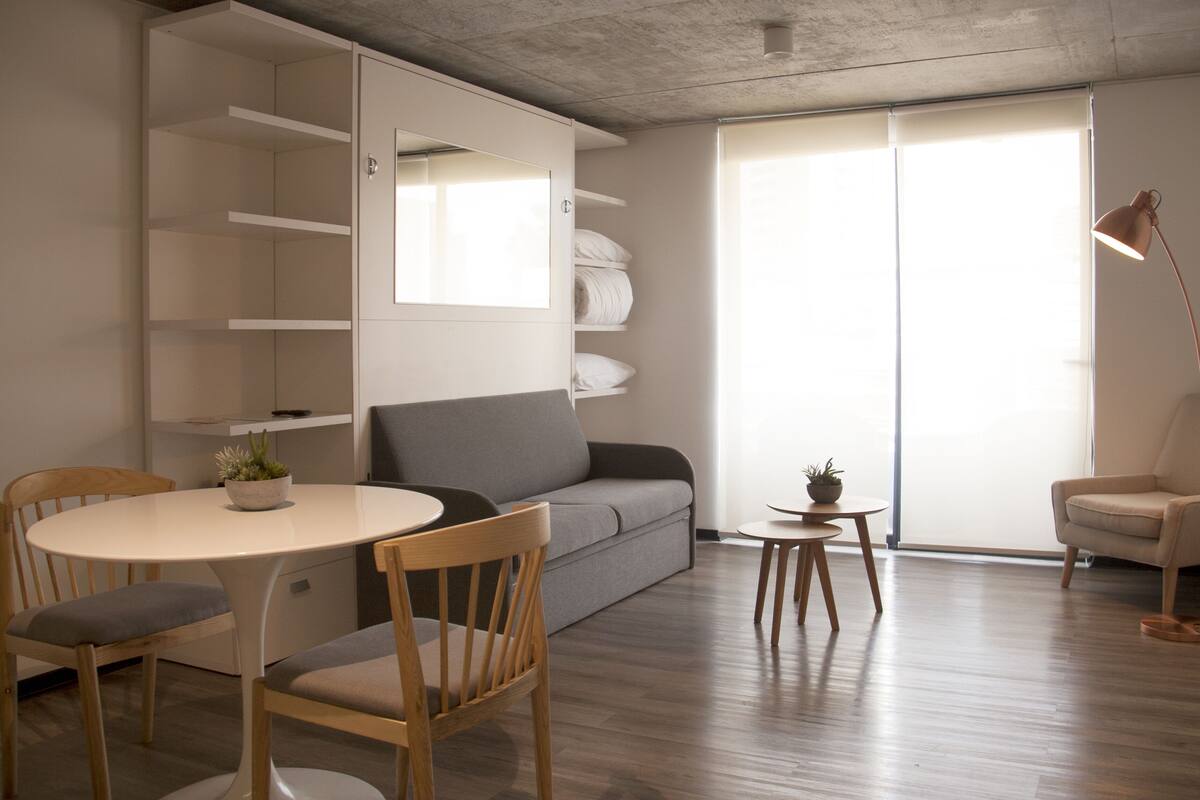 Una sala de estar moderna con un sofá, una mesa de comedor con sillas, una mesita auxiliar con una planta y una lámpara.