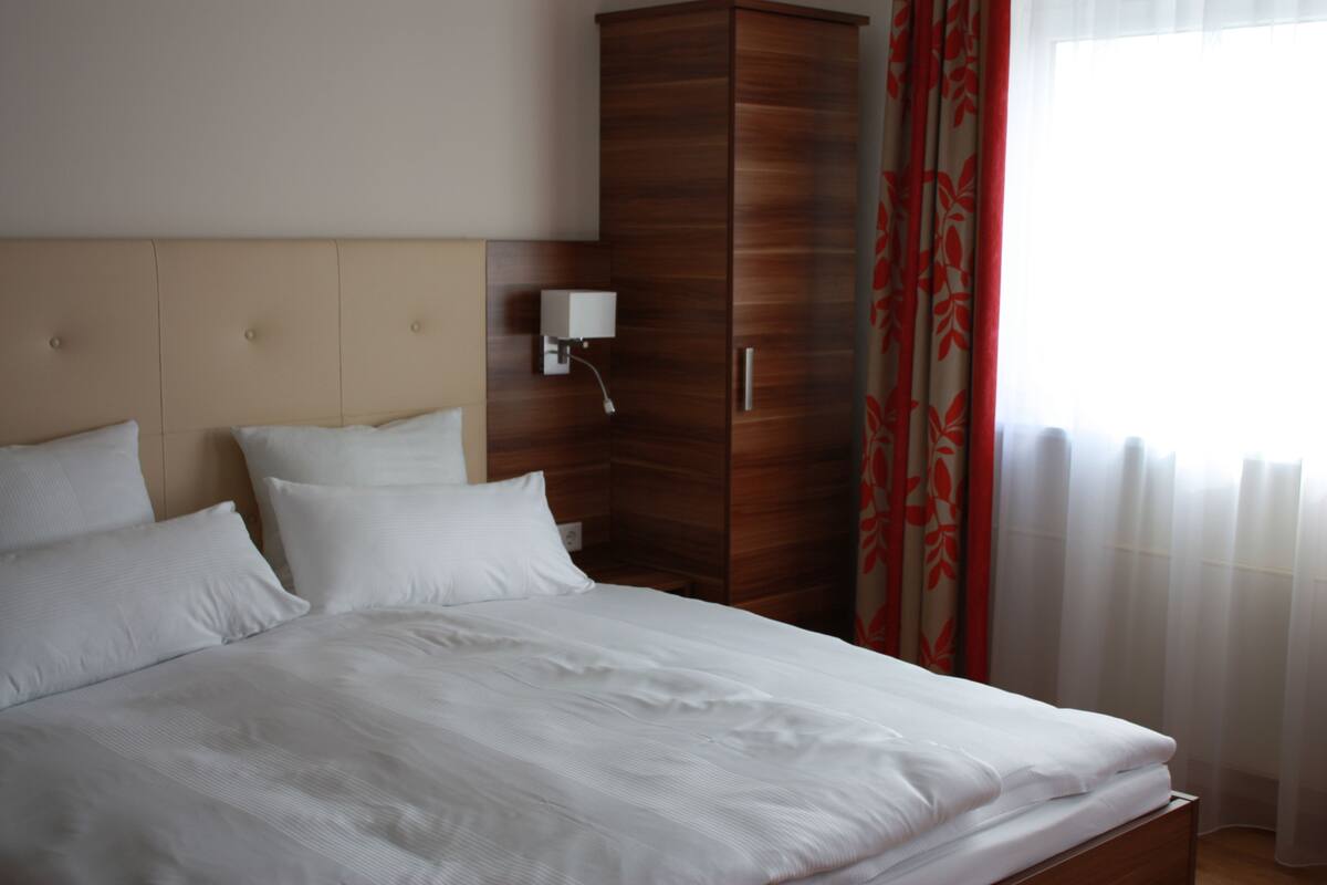 A neatly made bed with white linens, a wooden wardrobe, and a bedside lamp.