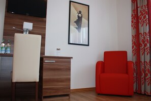 A room with a wooden desk, a red chair, a television mounted on the wall, and a framed picture. - Boardinghaus Holledau Inn (Schweitenkirchen)