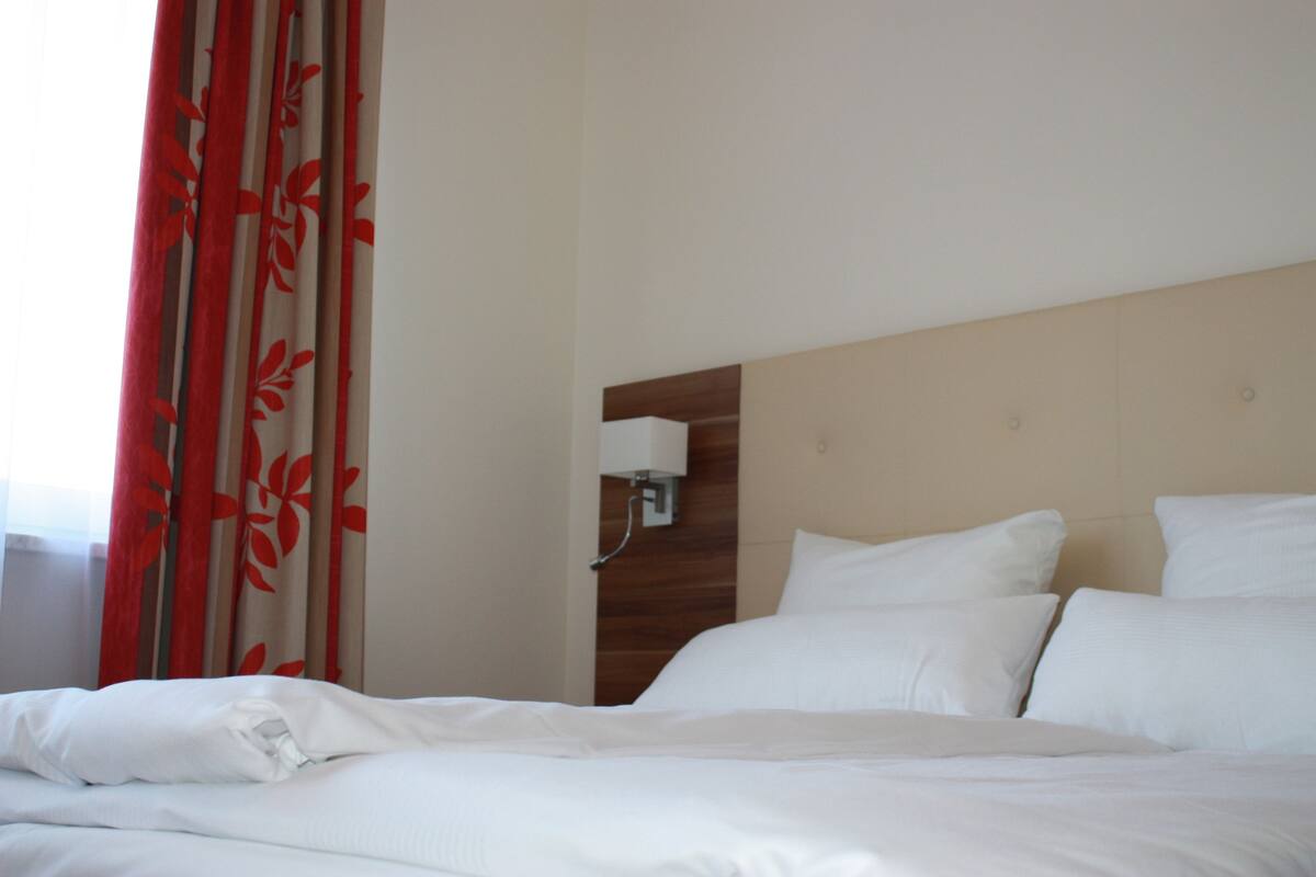 A hotel room with a bed, white bedding, a wooden headboard, and a wall-mounted light fixture.