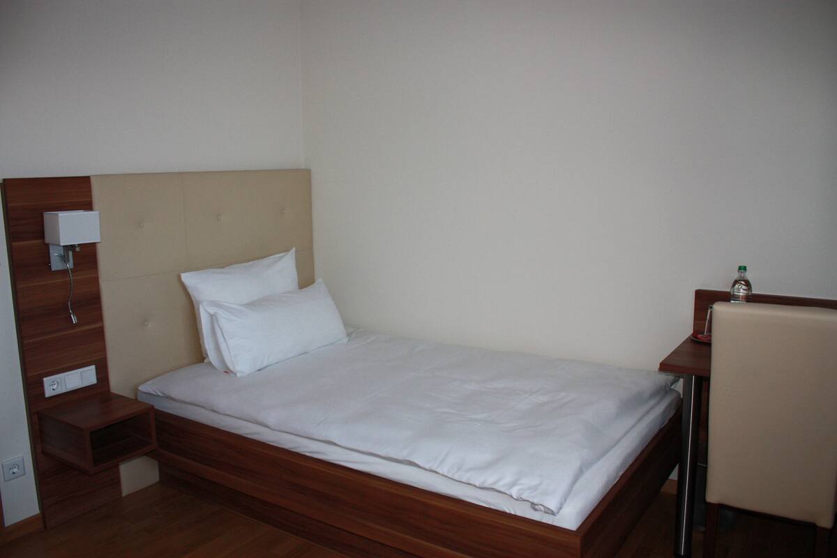A single bed with a wooden headboard, a bedside table, and a chair.