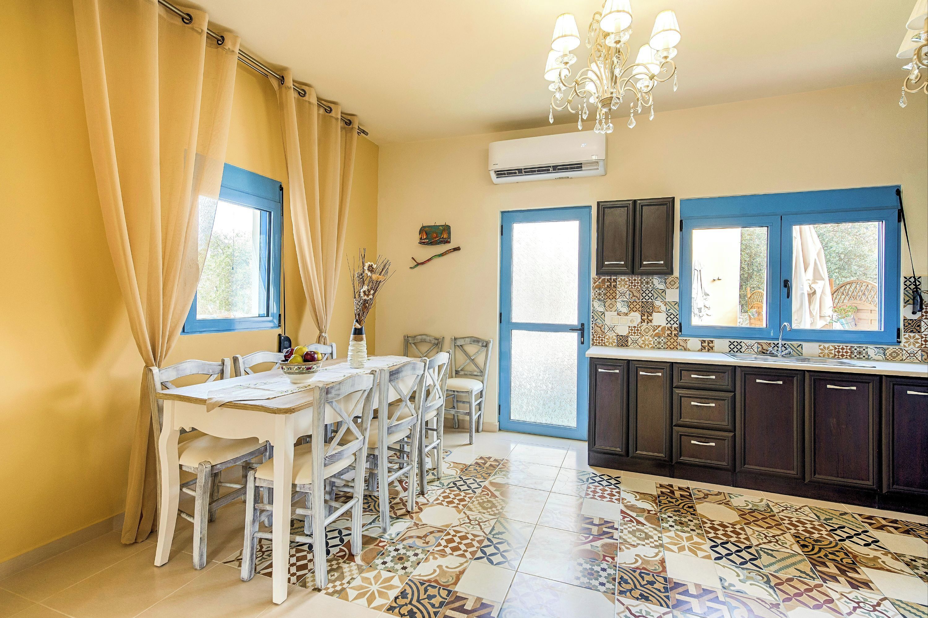 A kitchen with a dining area, featuring a patterned tile floor, a chandelier, and a blue-framed window.