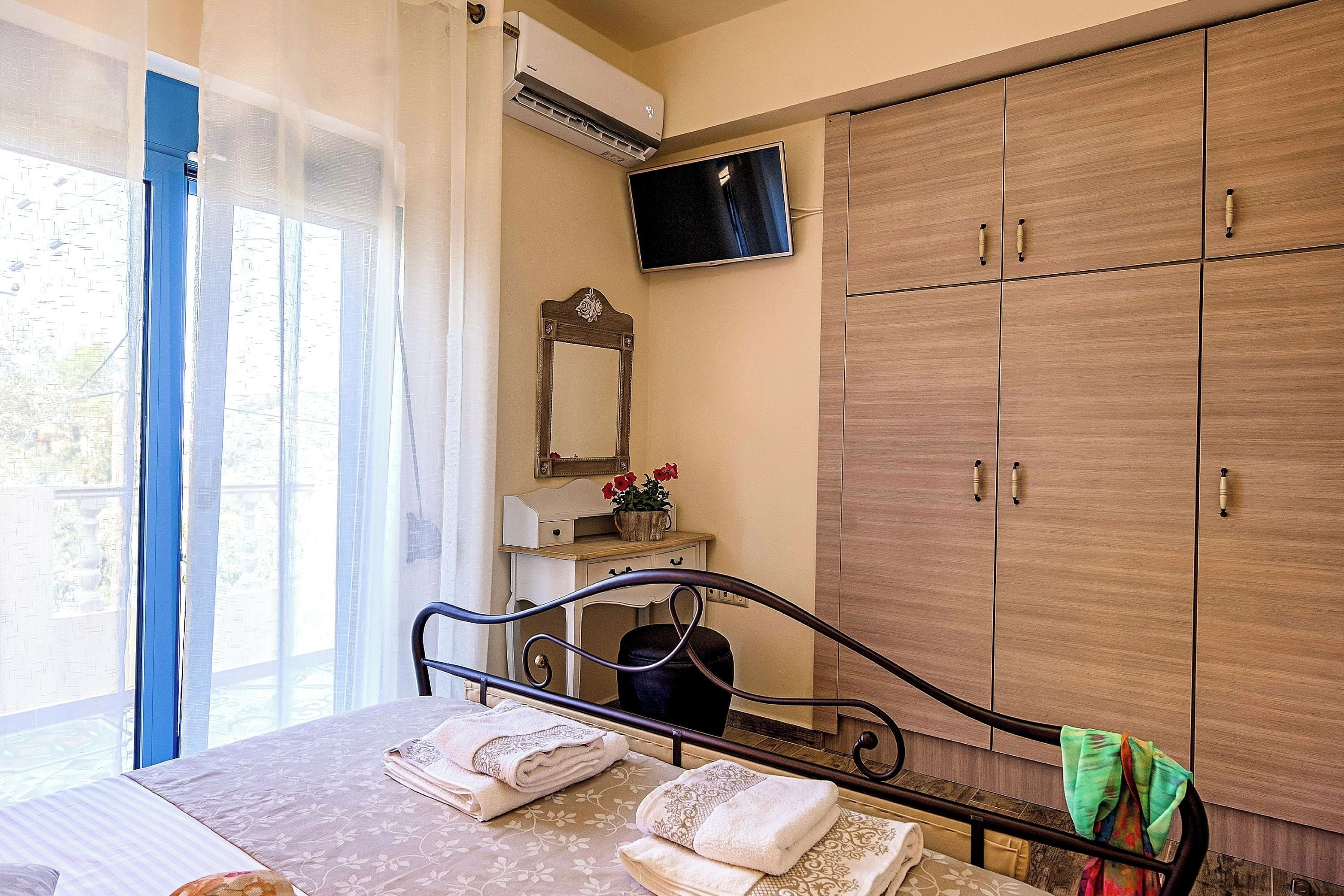 Une chambre à coucher avec un lit, un téléviseur fixé au mur, une armoire et une fenêtre avec des rideaux.