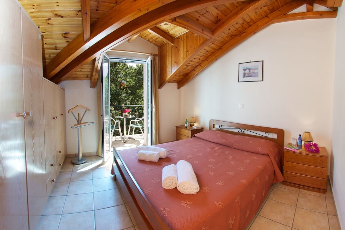 Un dormitorio con cama, mesita de noche, cómoda y ventana con vista a la vegetación.