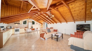 En rummelig loft lejlighed med højt til loftet og synlige træbjælker, et køkken med moderne hårde hvidevarer, et spiseområde og en opholdsstue med sofa og sofabord.