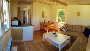 Una sala acogedora con piso de madera, una mesa de centro blanca, un sofá color crema y una mesa de comedor con sillas.