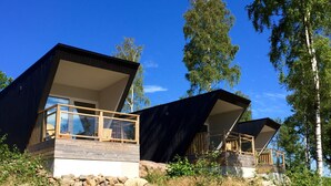 Una casa moderna de dos pisos con un balcón, rodeada de árboles y un muro de piedra.
