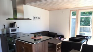 Cocina compacta con microondas, estufa y una isla grande. Cuenta con una zona de comedor con mesa y sillas, y un ventanal con vistas al exterior.