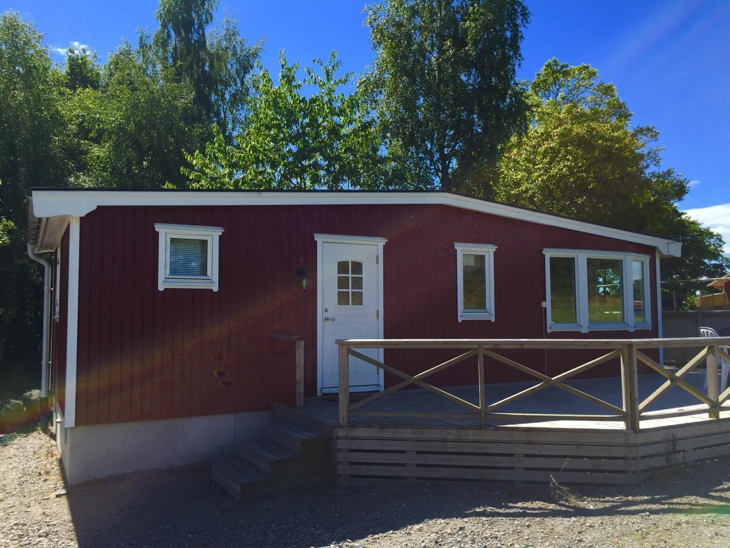 A red building with a white door and windows, a wooden deck, and a gravel ground.