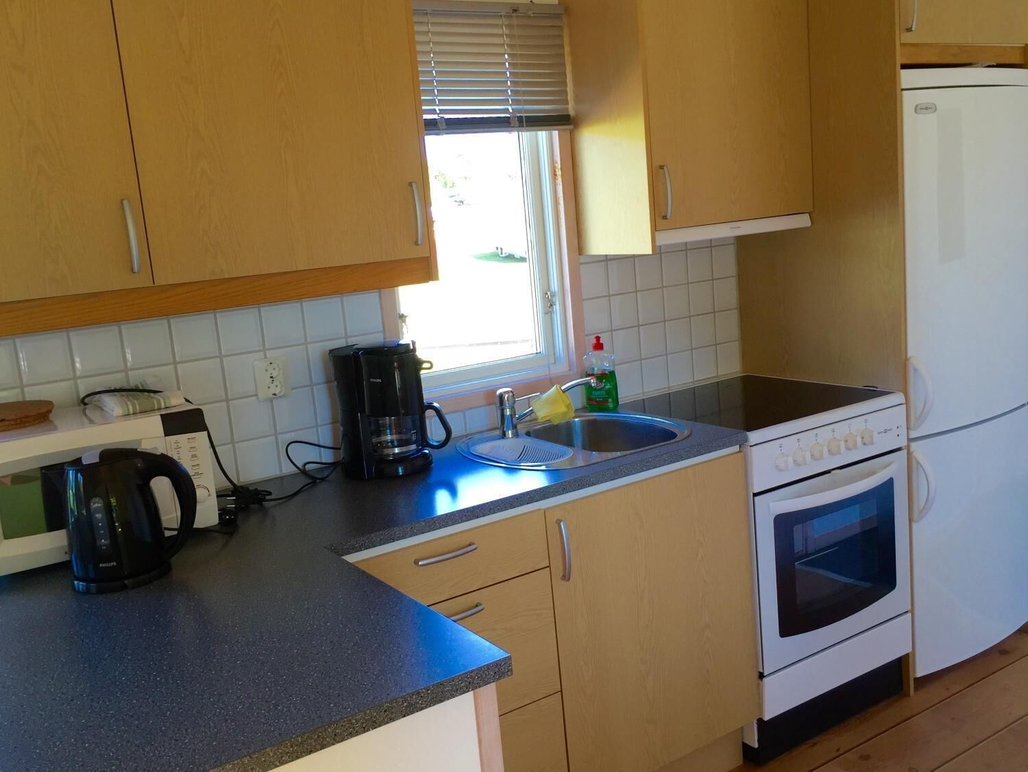 A compact kitchen with wooden cabinets, a built-in oven, a coffee maker, and a sink.