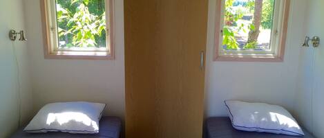 A room with two single beds, each with a pillow and a window.