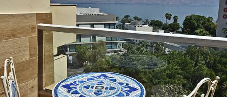A balcony with a tiled table and chairs, overlooking a body of water and distant hills.