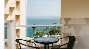 Ein Balkon mit Tisch und Stühlen mit Blick auf die Küste, Palmen und einen klaren Himmel.