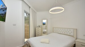 Quarto moderno com uma cama grande, mesa de cabeceira, espelho e vista para o exterior.