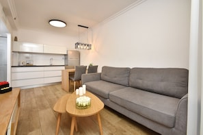A modern living room with a grey sofa, wooden coffee table, and a dining area with chairs and a table.