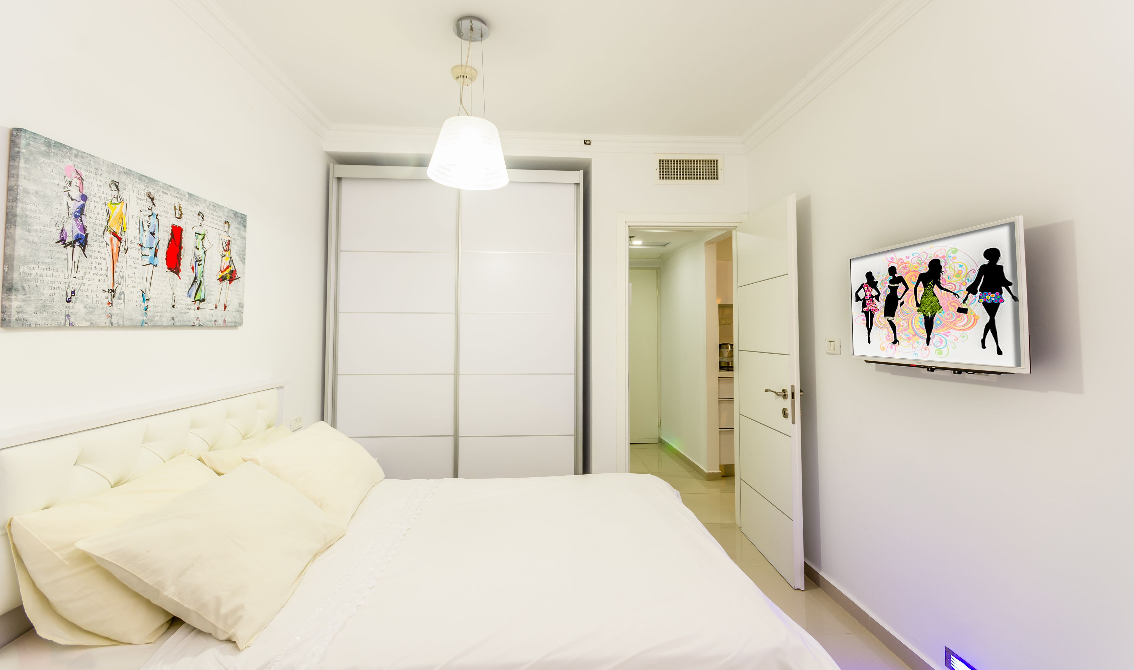 A bedroom with a bed, a wardrobe, and a hallway leading to a bathroom.