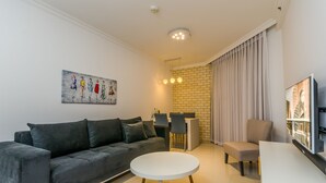 Uma sala de estar moderna com um sofá cinzento, uma mesa de centro branca e uma área de refeições com uma parede de tijolos e cortinas.
