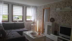 A living room with a sofa, coffee table, TV, and a decorative plant.