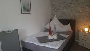 A neatly made bed with pillows and a blanket, a bedside table with a lamp, and a wall with a textured pattern.