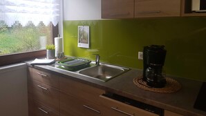 A kitchen with a green backsplash, wooden cabinets, a stainless steel sink, and a coffee maker on the counter.